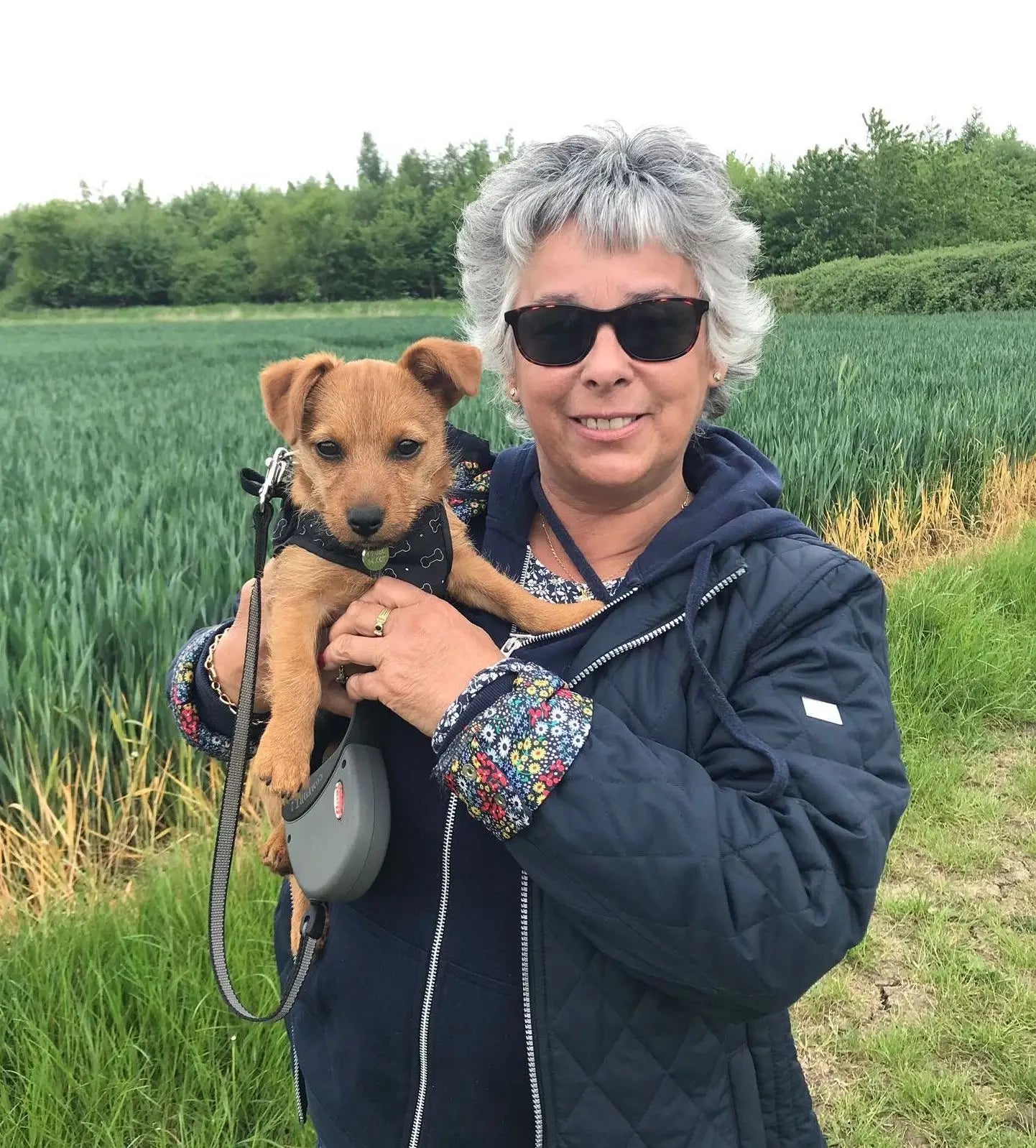 Woman holding a small dog in a field with greenery in the background
